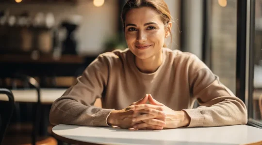 Portrait d'une personne sereine avec les mains posées naturellement sur une table de café, posture ouverte et relaxée