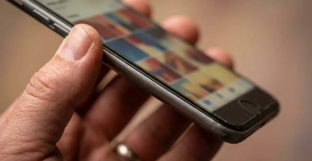 Main tenant un smartphone montrant une galerie photos floue avec des visages masqués